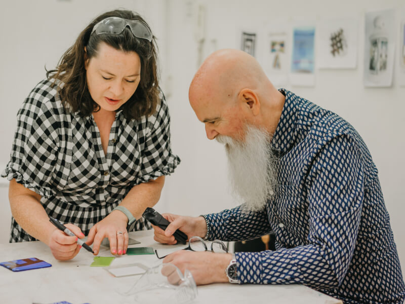 Two people create fused glass designs.